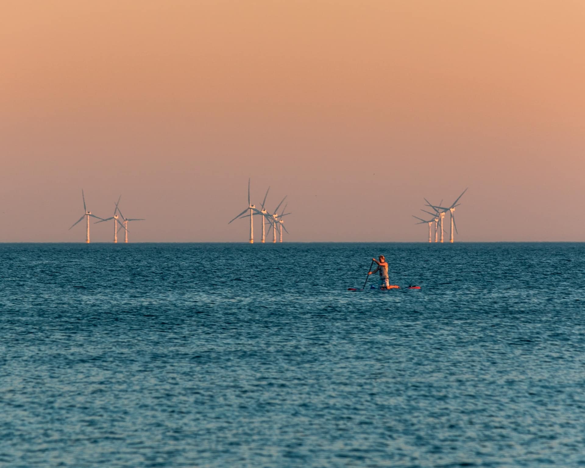 un parc d'éolienne en mer avec une personne en padel